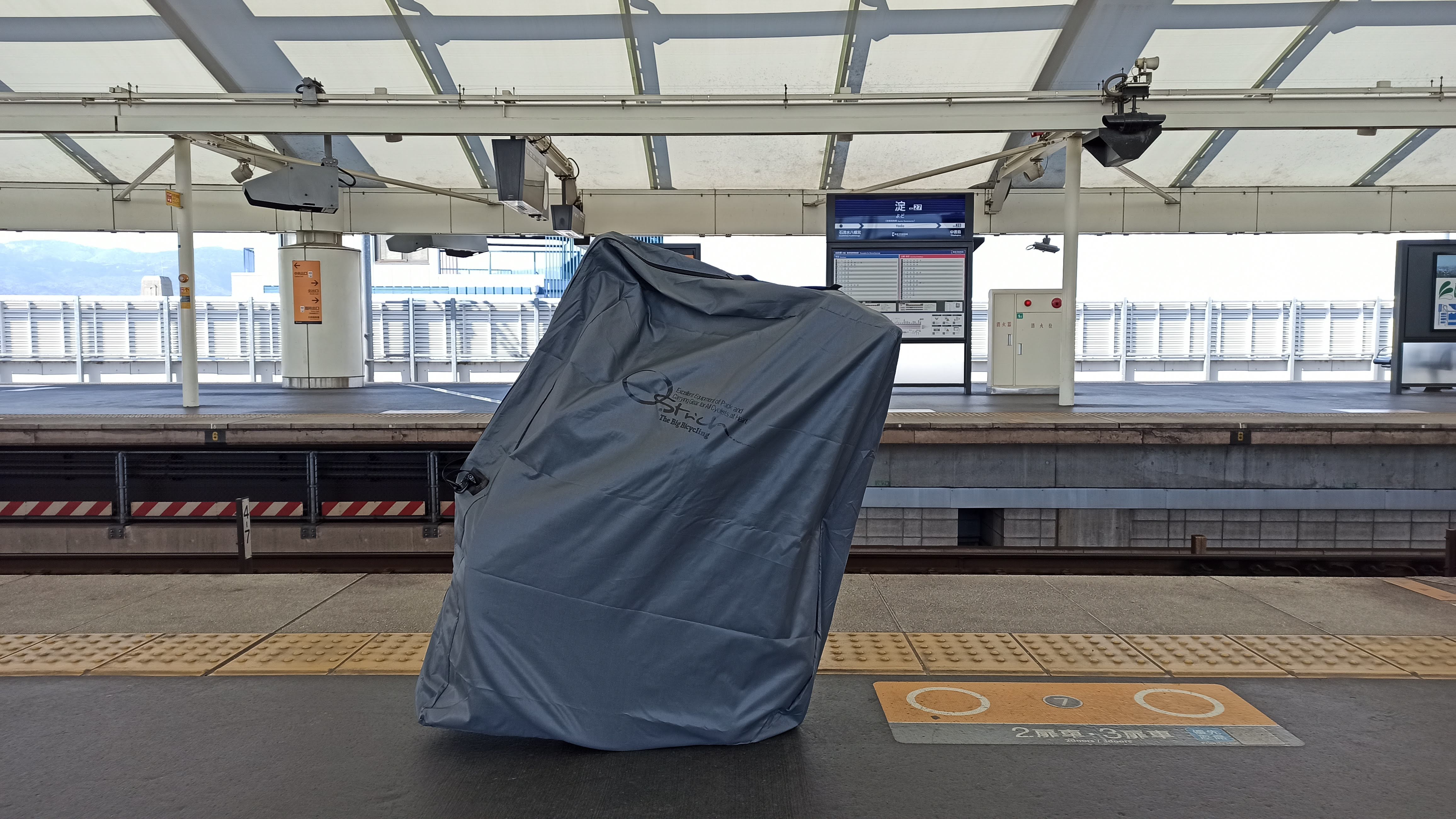 駅のホームに輪行袋に入ったロードバイクを置いた様子